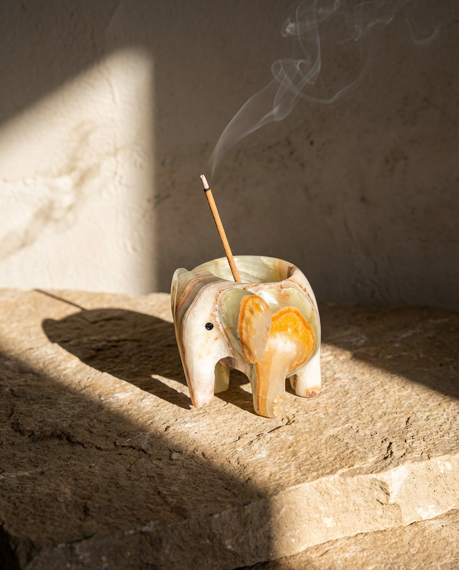 Ceramic elephant incense holder with a smoking incense stick on a stone surface.