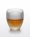Decorative glass with textured design and amber liquid on a white background