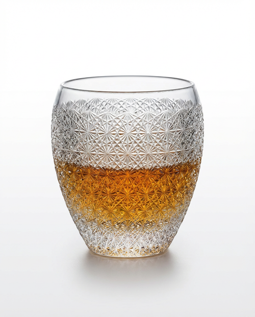 Decorative glass with textured design and amber liquid on a white background