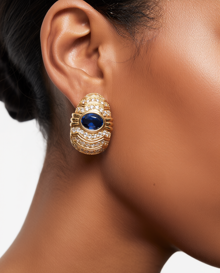 Gold earring with a blue gemstone worn by a person on a white background
