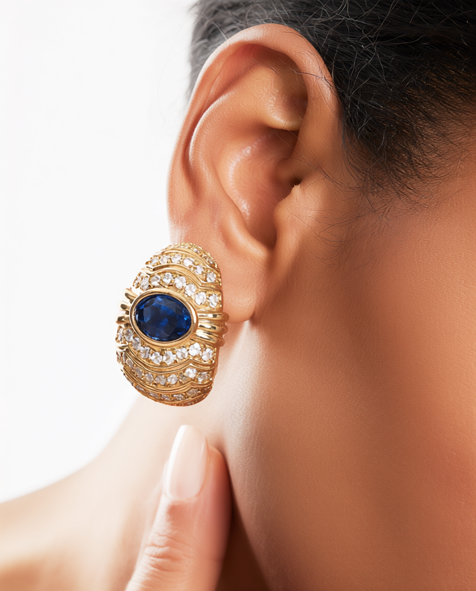 Gold earring with a blue gemstone worn by a person