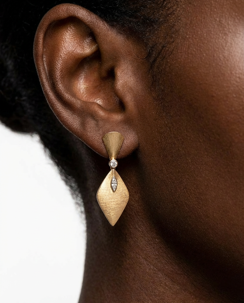 Close-up of an ear wearing a gold earring with a clear gemstone on a white background