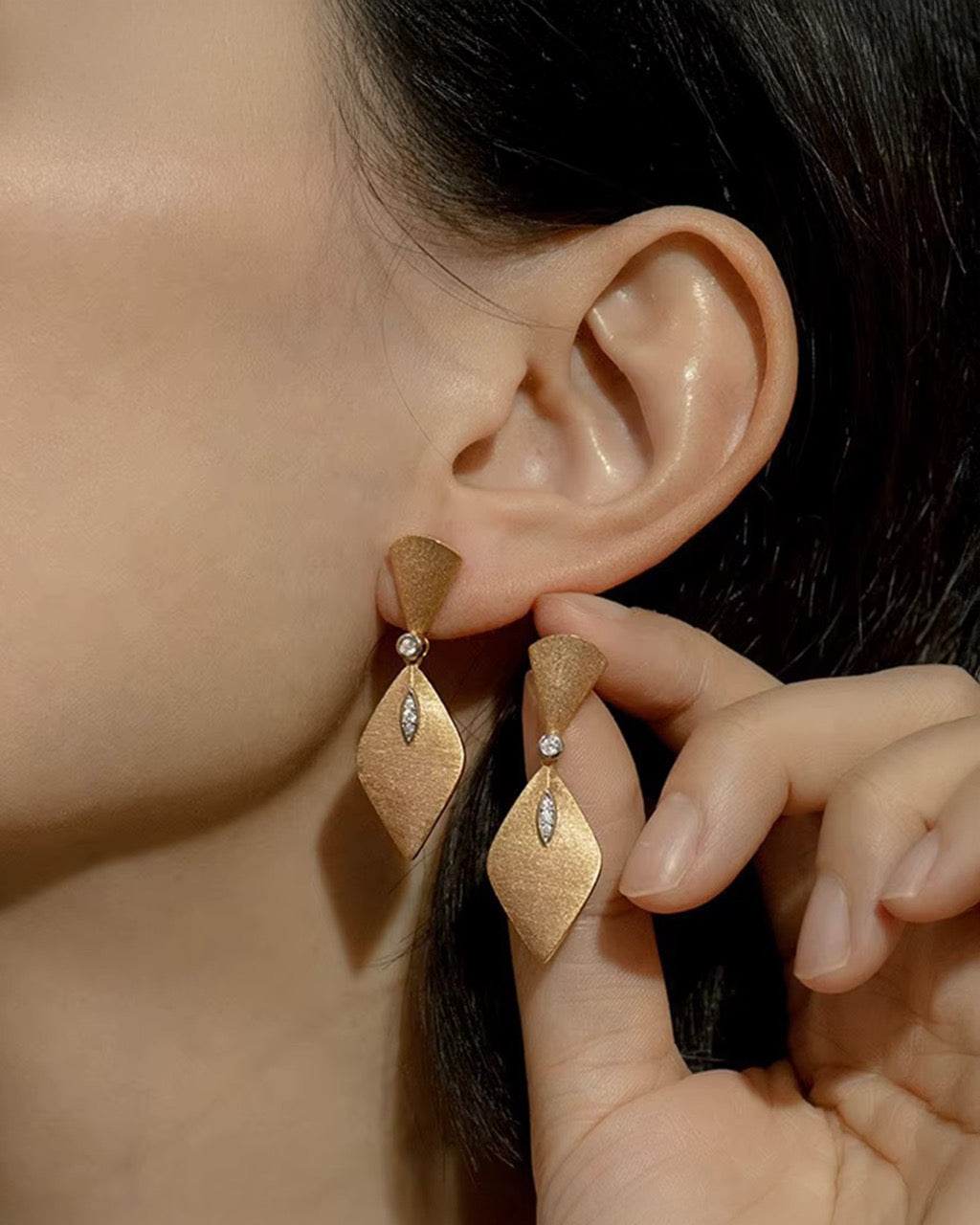 Gold earrings being worn with a blurred background