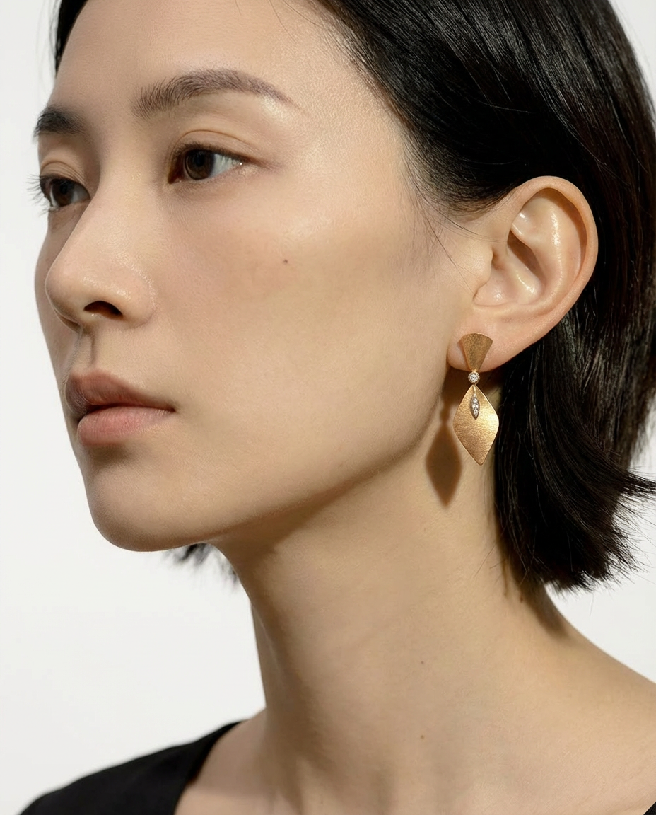 Close-up of a person wearing a gold earring with a clear gemstone on a plain background