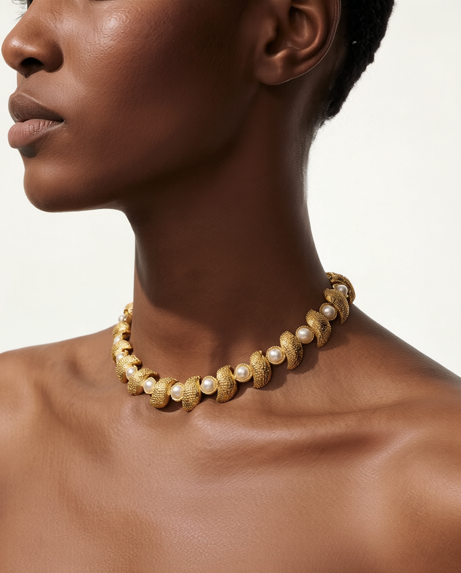 Close-up of a person wearing a gold and pearl necklace against a neutral background