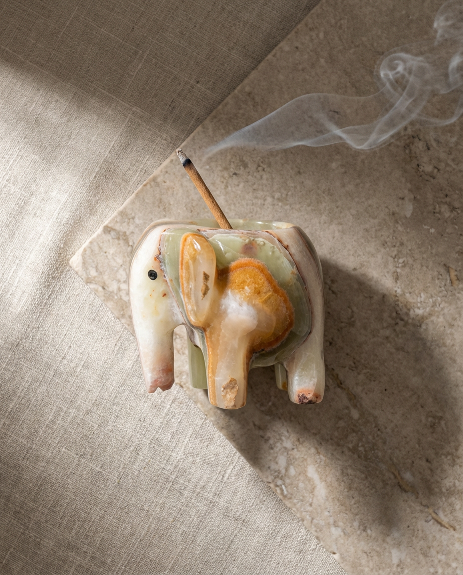 Elephant-shaped incense holder with a burning incense stick on a textured surface