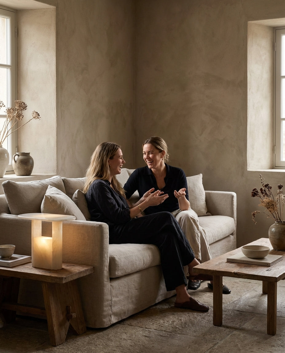 Two women sitting on a couch in a cozy living room with soft lighting.