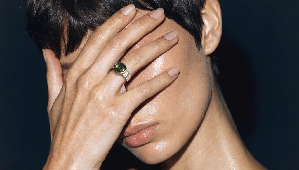 Person with a ring on their finger covering their face against a dark background