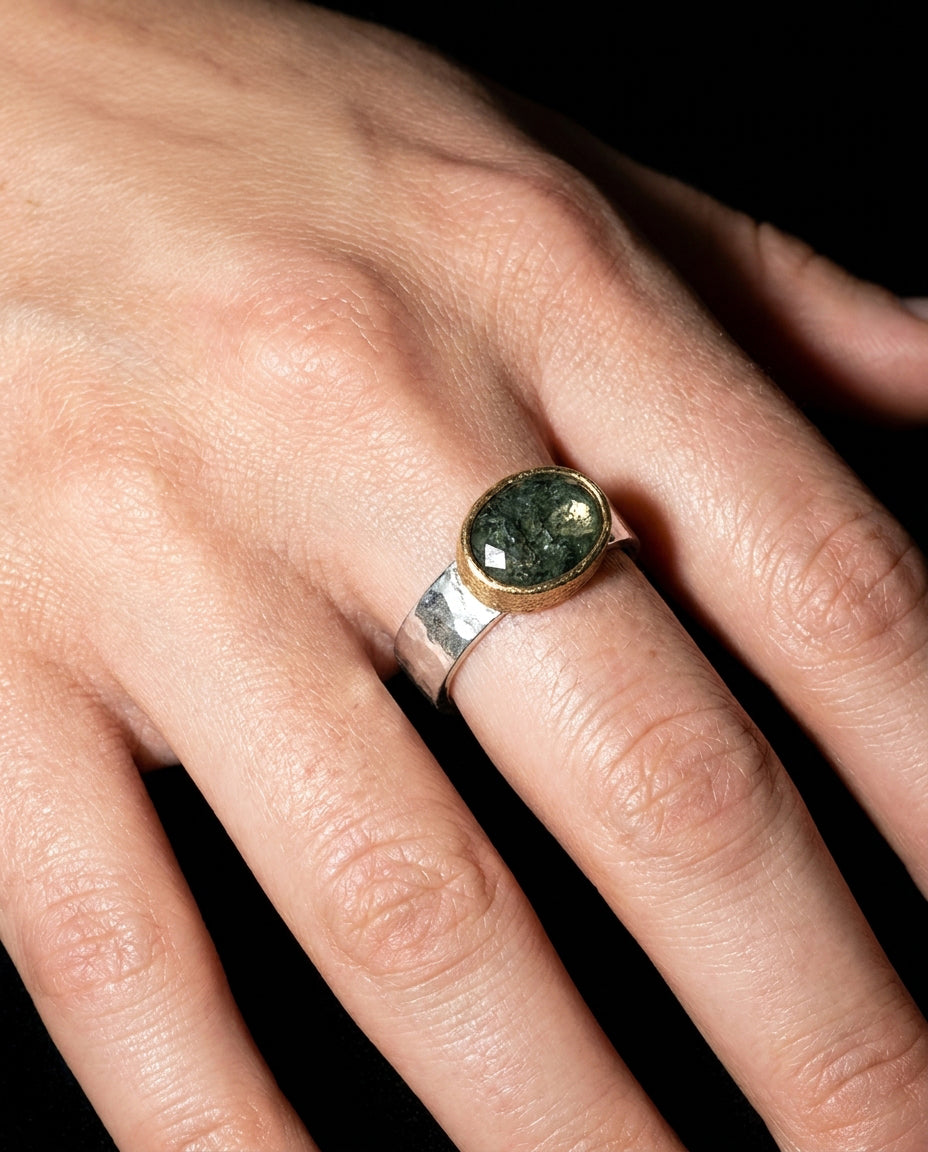 Hand wearing a ring with a green stone on a dark background