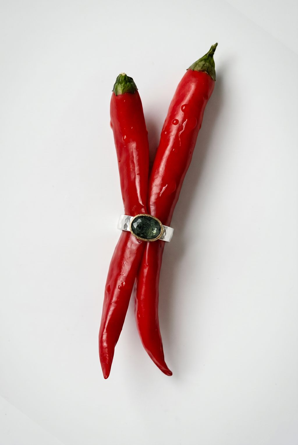 Two red chili peppers with a silver ring on a white background