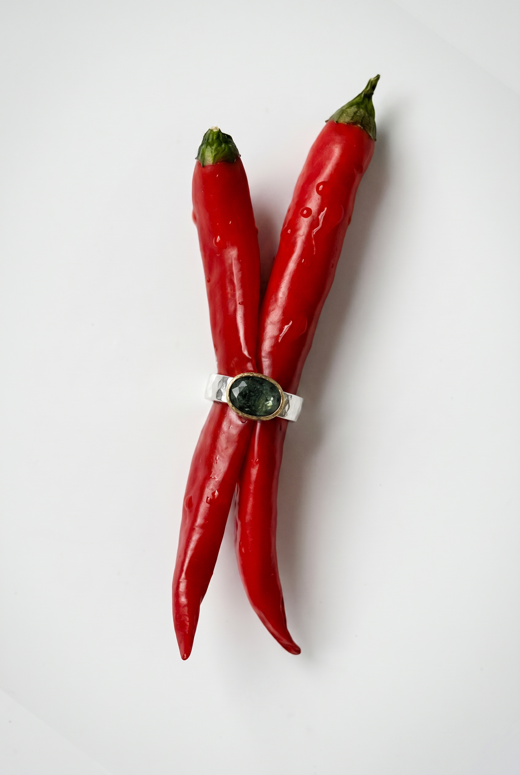 Two red chili peppers with a silver ring on a white background