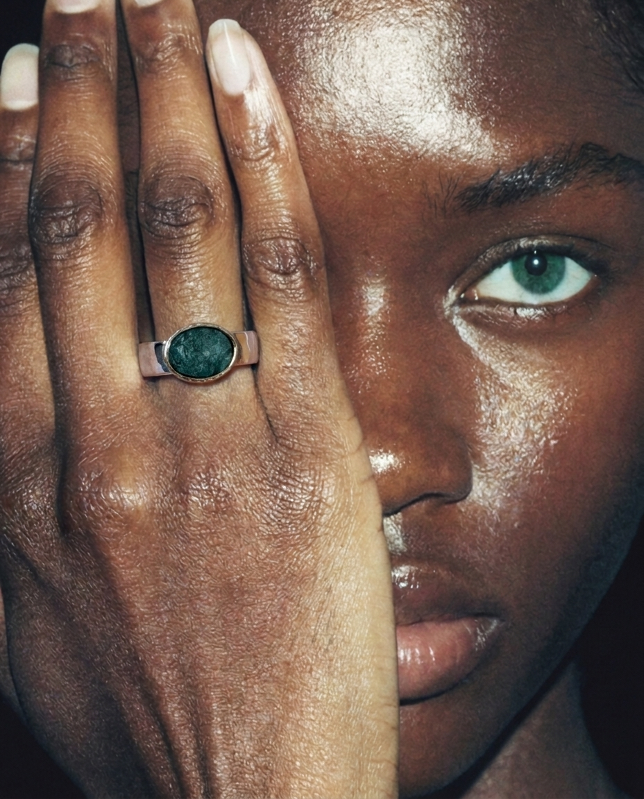 Close-up of a person's hand with a ring featuring a green gemstone, held near the face.