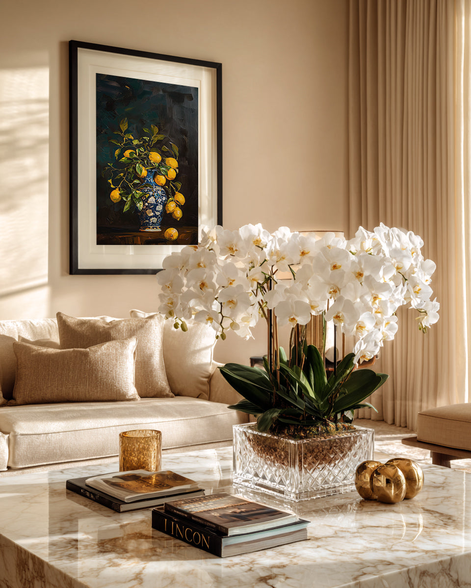 Living room with a white orchid arrangement on a marble table, framed artwork on the wall, and a beige sofa.