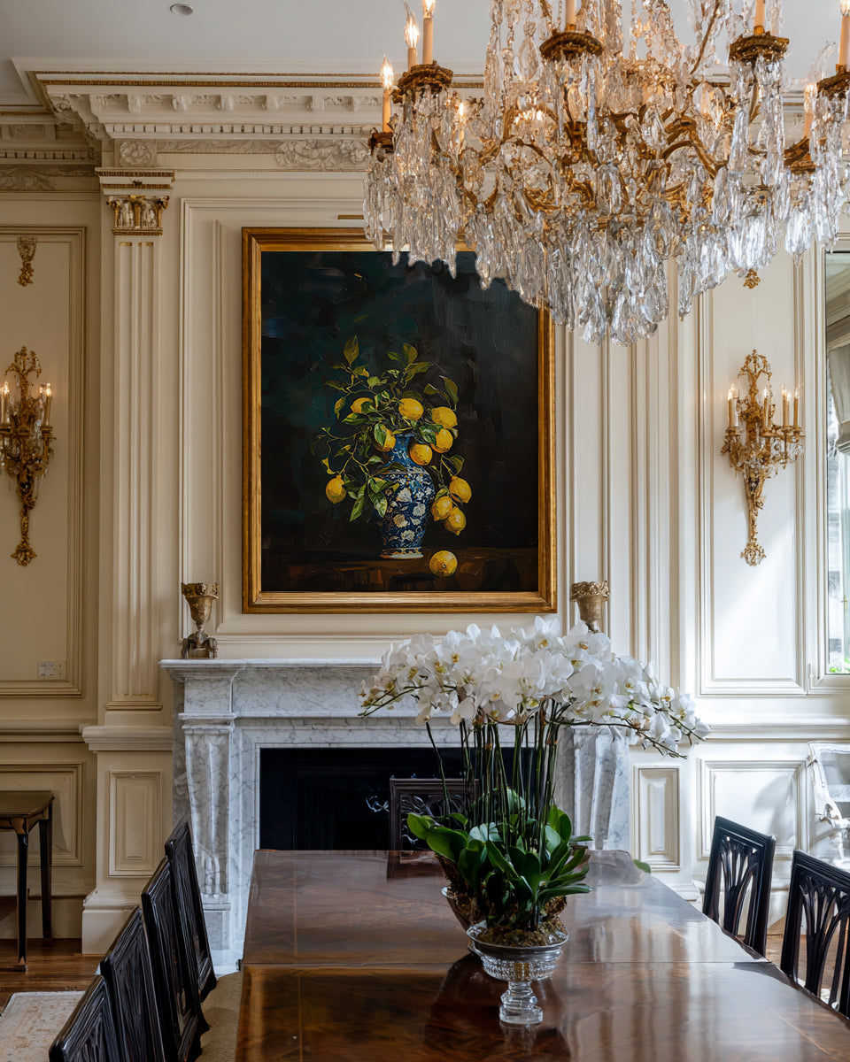 Dining room with a large chandelier, painting of lemons, and floral arrangement.
